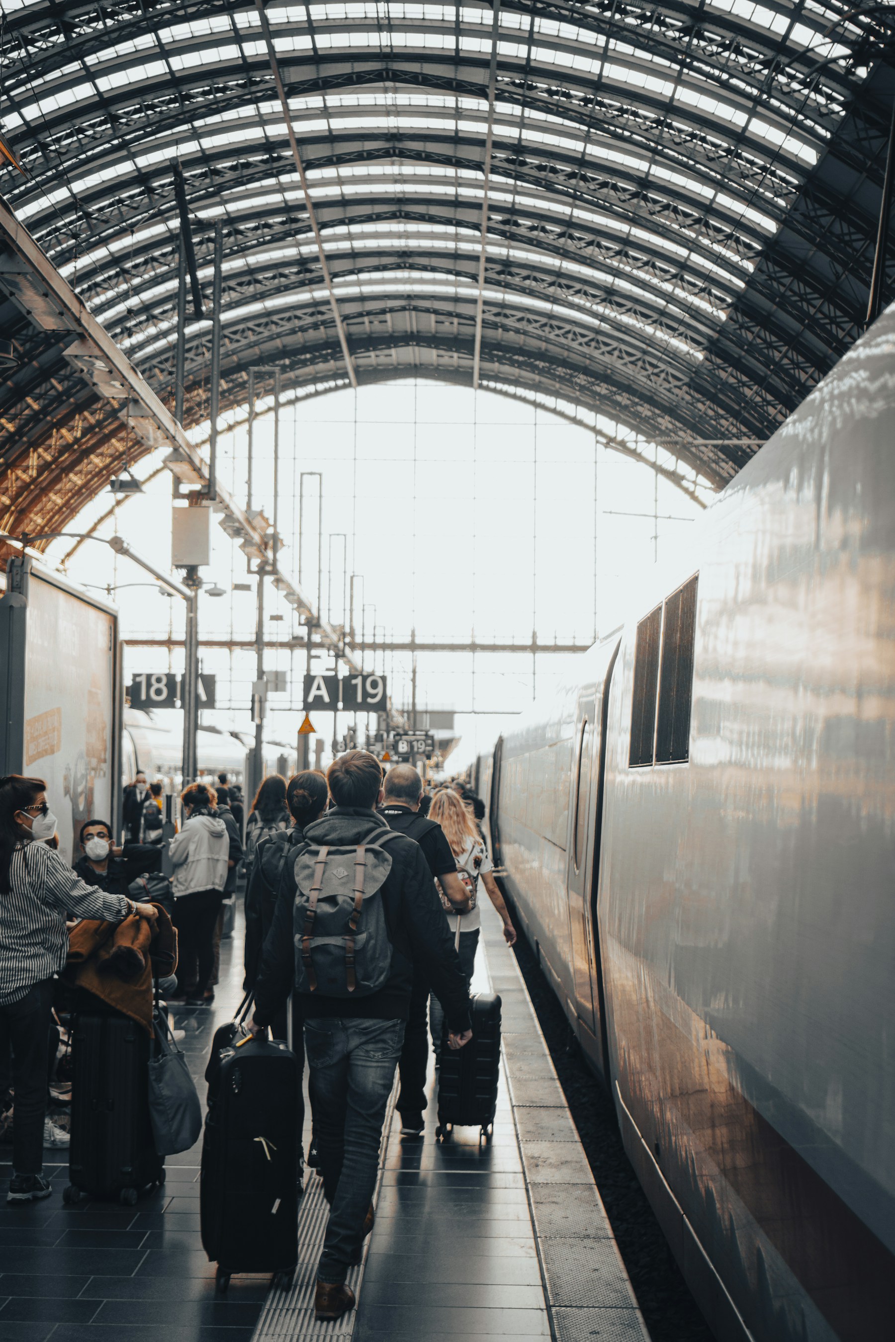 Travelers with rolling luggage on a platform beside a train