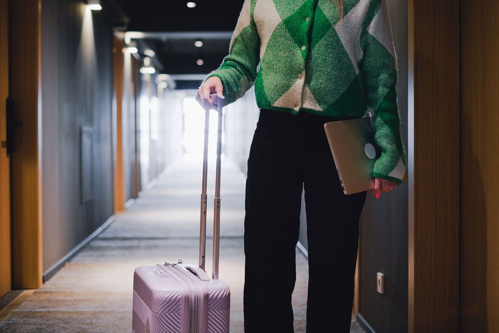 Person carrying a laptop and rolling luggage in a hotel corridor